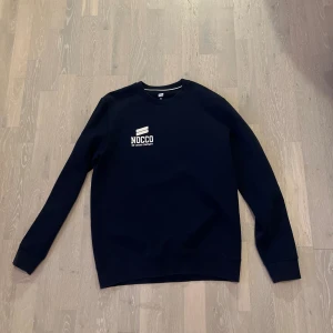 Nocco sweatshirt - Säljer en mörkblå sweatshirt från NOCCO med vit logga tryckt på både bröstet och ryggen. Tröjan har rund hals, långa ärmar och är tillverkad i mjukt material som passar perfekt för en chill stil.