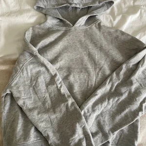 Grå hoodie från H&M Divided - En klassisk grå hoodie från H&M Divided i mjuk bomullsblandning. Tröjan har huva, långa ärmar och ribbade muddar vid ärmslut och nederkant. Perfekt för en chill och avslappnad stil.