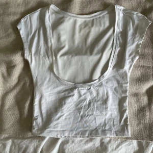 Vit croppad topp från Bik Bok - Säljer en vit croppad topp från Bik Bok i mjuk bomull. Toppen har korta ärmar och en djup, öppen rygg som ger en snygg och modern look. Perfekt att styla med jeans eller kjol för en fräsch vibe.