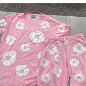Rosa shorts från Denim Tears med blommor - Säljer ett par rosa shorts från Denim Tears med vita blommiga mönster över hela tyget. De har en relaxed fit, resår i midjan och snörning framtill. Perfekta för en chill vibe och sticker verkligen ut med sitt unika tryck.