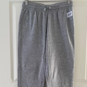 Grå mjukisbyxor med snörning - Säljer ett par grå mjukisbyxor från Daily Paper med elastisk midja och snörning. Byxorna har en avslappnad passform och är tillverkade i mjukt bomullsmaterial. Perfekta för chill dagar eller när du vill vara extra bekväm.