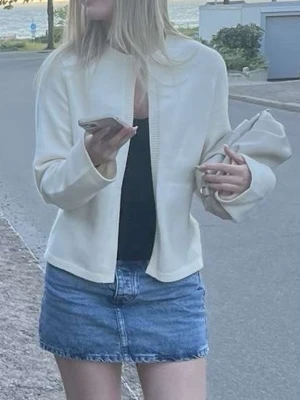 Vit kofta med ribbad kant - Säljer en stilren vit kofta med ribbad kant framtill. Koftan har lång ärm och är i ett mjukt material som passar perfekt till jeans eller kjol. Enkel och clean design utan knappar eller dragkedja, vilket gör den lätt att matcha med olika outfits.