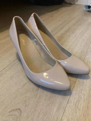 Beige pumps med låg klack - Snygga beige pumps från Alley med glansig finish och spetsig tå. Skorna har låg klack och klassisk siluett som passar till många olika looks. Tillverkade i syntetmaterial med mjuk innersula för extra komfort.