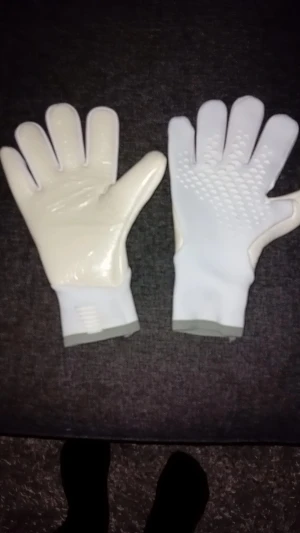 Vita målvaktshandskar med grepp - Säljer ett par vita målvaktshandskar med grå kant vid handleden. Handflatan är slät och glansig medan ovansidan har mönstrade greppzoner för bättre bollkontroll. Handskarna har en sportig look och är perfekta för fotbollsträning eller match. Helt nya med plast.