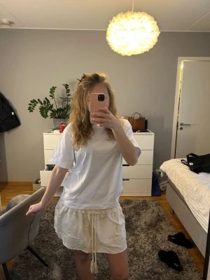 Beige kjol från Zara - Supersöt beige kortkjol från Zara med smock i midjan, volangkant och snörning med tofsar. Kjolen är i storlek S och har en lätt struktur i tyget och känns luftig och perfekt för varma dagar. Det finns ingen lapp på den.