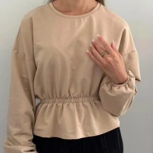 Beige långärmad tröja från NA-KD - Säljer en beige croppad, långärmad tröja med volangdetalj och resår i midjan från NA-KD i XXS.  Oanvänd.