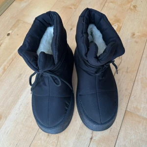 Svarta fodrade boots med snörning - Säljer ett par svarta boots med tjock platt sula och snörning framtill. Skorna är vadderade och har ett mjukt, vitt foder på insidan som håller fötterna varma. Perfekta för kalla dagar och har en chunky look. Endast använda en gång och därför i mycket bra skick. Original-sula saknas men är utrustade med liknande fodrade sulor. 