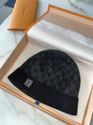 Louis Vuitton svart rutig mössa - Säljer en svart mössa från Louis Vuitton med diskret rutigt mönster och LV-logga framtill. Mössan har en bred kant och är tillverkad i mjukt material som känns lyxigt och stilrent. Perfekt accessoar för dig som vill ha något exklusivt och snyggt.