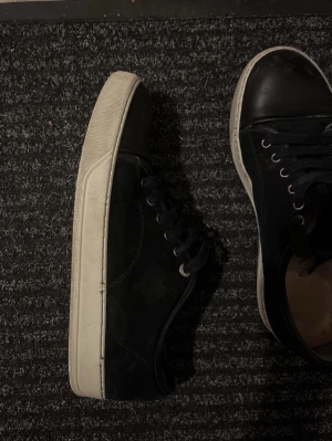 Lanvins - Säljer ett par svarta sneakers med vit platt sula och snörning. Skorna har en klassisk rund tå och är perfekta för dig som gillar stilrena och enkla skor. Passar till jeans eller andra avslappnade outfits.