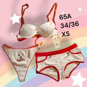 Snoopy underklädesset  - Supergulligt Snoopy-set med bh och två olika trosor (string och hipster) i vitt med röda detaljer. Bh:n har orange axelband med Snoopy-tryck och båda trosorna har Snobben-motiv. Materialet är mjuk bomull med lite stretch för extra komfort. Storlek 65A, 34/36 och XS. Från ett konkurslager från 2000-talet kommer dessa retro stringtrosor med Snobben på. Tunna i tyget. I övrigt enligt bilden. Oanvända såklart med orginallapparna kvar. Finns fler storlekar, bara fråga. Rejäl bundlerabatt.