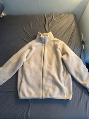 Beige fleecejacka med dragkedja uniqlo S - Mysig beige fleecejacka med hög krage och hel dragkedja framtill. Perfekt för kyliga dagar och enkel att slänga på sig över en t-shirt. Jackan har en clean look utan synliga loggor eller detaljer.