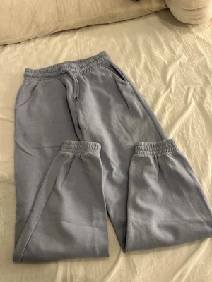 Grå mjukisbyxor från Lindex - Grå mjukisbyxor från Lindex med elastisk midja och snörning. Byxorna har fickor på sidorna och texten 'TODAY TOMORROW' tryckt på ena benet. Tillverkade i mjukt bomullsmaterial, perfekta för chill dagar.