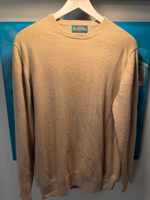 Beige cashmeretröja från Alan Paine - Säljer en stilren beige rundhalsad tröja från Alan Paine i 100% kashmir. Tröjan har en klassisk passform med ribbade muddar vid ärmslut och nederkant. Perfekt för dig som gillar mjuka och lyxiga material. Storlek 44 UK 52 EU. Men Alan Paige har mycket små storlekar så skulle säga Medium
