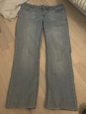 Blå bootcut jeans med slitna detaljer - Säljer ett par ljusblå Levi's jeans med bootcut passform. Jeansen har klassisk femficksdesign, dragkedja och slitna detaljer vid midjan och benslut. Materialet är jeans och färgen har en snygg tvättad look. Perfekt för dig som gillar retrostil och bredare ben. OBS knapp saknas 