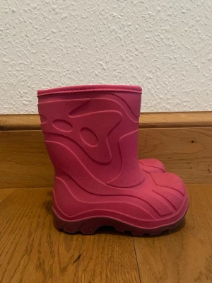 Rosa fodrade vinterstövlar barn - Säljer ett par rosa vinterstövlar för barn med grov sula och mjukt grått foder på insidan. Stövlarna är tillverkade i syntetmaterial och har en cool, mönstrad yta som ger extra stilpoäng. Perfekta för kalla dagar när du vill hålla fötterna varma.