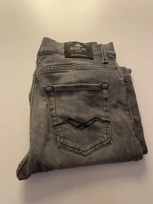 Grå Replay jeans, rak modell - Säljer ett par grå jeans från Replay i rak modell. Klassisk femficksdesign med Replay-logga på bakfickan och etikett bak i midjan. Jeansen är i mjukt denimtyg och har snygga slitningar för en avslappnad look. Passar dig som gillar stilrena och tidlösa jeans.