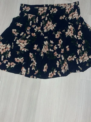 Blommig kortkjol i mörkblått - Supersöt mörkblå kortkjol med blommor från Vero Moda! 🌸 Kjolen har en lätt utställd form och resår i midjan för skön passform. Perfekt för dig som vill ha en fräsch och somrig vibe i garderoben. 😍 Storlek xs, sparsamt använd men fint skick! 💕