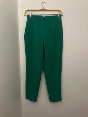 Gröna kostymbyxor från Zara M - Snygga gröna kostymbyxor från Zara i storlek M. Byxorna har hög midja, raka ben och diskreta fickor framtill. Materialet känns mjukt och har en lätt stretch, perfekt för en clean och stilren look.