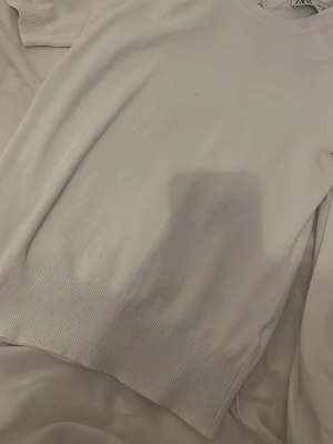 Kortärmad stickad tröja - Vit tröja från Zara i storlek S med rund hals och tre dekorativa guldfärgade knappar vid halsen. Tröjan har kort  ärm och ribbad kant nedtill. Mjuk och skön känsla, perfekt för dig som gillar enkel och stilren look.