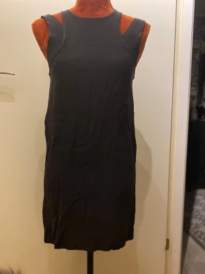 Svart ärmlös kortklänning 36/38 - Svart klänning med speciella axelband och dragkedja baktill. Liten i storlek (36) 51% silke, 49% viskos Foder 100% polyester Längd: 85 cm, bystmått: 41 cm  Inga bilder när den sitter på mig! Katter finns i hemmet! Kan ej skicka med UPS!