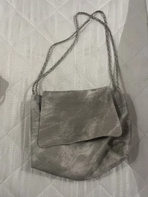 Grå axelväska i sammet med kedjerem - Säljer en snygg grå axelväska i mjuk sammet med kedjerem. Väskan har ett lock och en stilren, enkel design som passar till många olika outfits. Perfekt storlek för det viktigaste och ger en cool touch till din look. Oanvänd och ny - tyckte inte den passade med mina outfits !