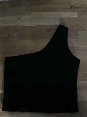 Svart oneshoulder topp XS - Säljer en svart ribbad oneshoulder topp i storlek XS. Toppen är ärmlös och har en asymmetrisk design med en axel. Perfekt för dig som gillar stilrena och trendiga plagg. Materialet är mjukt och stretchigt för en bekväm passform.