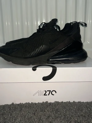 Nike Air 270 helsvarta sneakers - Säljer ett par helsvarta Nike Air 270 sneakers med snygg mesh-överdel och stor synlig luftkudde i hälen. Skorna har snörning och en platt sula med rund tå. Perfekta för dig som gillar sportig stil och vill ha något som funkar till streetwear.