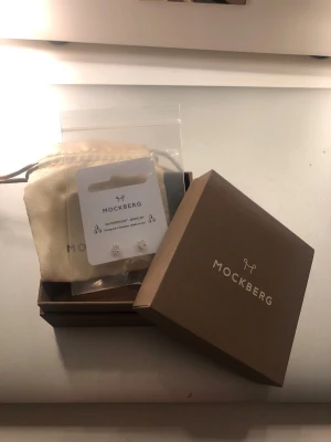 Örhängen - Säljer ett par kristallörhängen från Mockberg, ”Jolie Gold Medium Stud - White”. Aldrig använd! Vattentåliga. Ord. pris 399 kr.