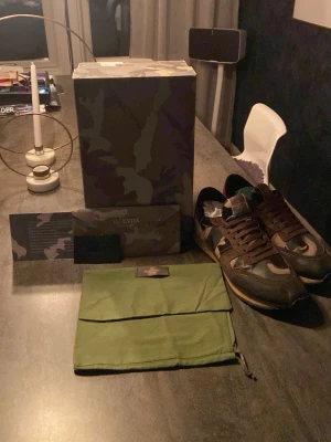 Valentino Rockrunners - Säljer ett par Valentino Rockrunner sneakers med snyggt camouflage-mönster i grönt, brunt och beige. Skorna har detaljer i skinn och mocka, platt sula och rund tå. Man får även med ett valentino armband vid köpet