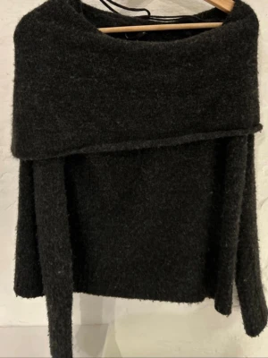 Mörkgrå offshoulder stickad tröja - Mysig mörkgrå stickad tröja med bred offshoulder-krage och långa ärmar. Perfekt för kyliga dagar när du vill ha något både snyggt och bekvämt. Tjockt material som känns riktigt gosigt.