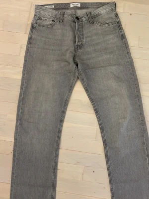 Grå jeans från Jack & Jones Relaxed/Chris - Säljer ett par grå jeans från Jack & Jones, modellen Relaxed/Chris. De har en avslappnad passform med raka ben och klassisk femficksdesign. Jeansen är tillverkade i jeansmaterial och har knapp och dragkedja framtill samt bälteshällor.