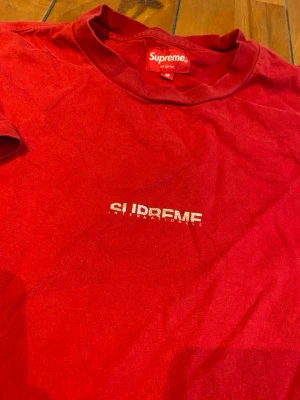 Röd Supreme t-shirt med tryck - Supreme t-shirt i rött med diskret Supreme International tryck på bröstet. Klassisk rund hals och korta ärmar. Gjord i 100% bomull för skön och mjuk känsla. Perfekt för dig som gillar streetwear och vill ha något enkelt men ändå ikoniskt.