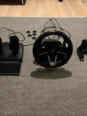 HORI Racing Wheel Apex - HORI Racing Wheel Apex för PlayStation med pedaler och fästen. Komplett set med USB-anslutning, kompatibel med PS4, PS5 och Dator. Ratt och pedaler i fint skick, inga synliga defekter eller slitage. Perfekt för realistisk racingupplevelse hemma.