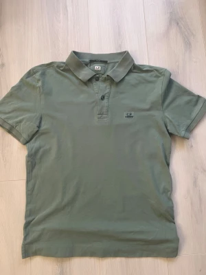 C.P. Company pike (äkta) - Säljer en grön piké från C.P. Company med klassisk pikékrage och två knappar framtill. Slim fit-modell med korta ärmar och diskret logga broderad på bröstet. Storlek S, skick 8/10 inga synliga defekter. Kontakta mig om du har frågor!