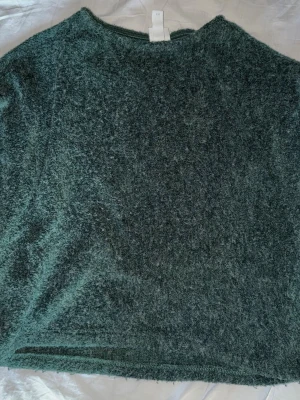 Mörkgrön stickad tröja - Mysig mörkgrön stickad tröja med enkel design och rund hals. Materialet är fluffigt och ger en skön känsla mot huden. Perfekt för att hålla värmen under kyliga dagar. Passar dig som gillar en avslappnad och stilren look.