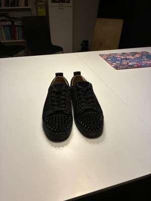 Christian Louboutin skor  - Säljer ett par äkta Christian Louboutin i mocka med coola svarta nitar över tån. Skorna har snörning och en platt sula. Insidan är beige och de har en stilren, edgy look som sticker ut. Perfekta för dig som vill ha något extra till outfiten. Skriv för fler frågor om skorna. Skorna är i storlek 41 men kan passa 42