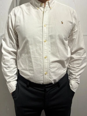 Vit skjorta Ralph Lauren - Klassisk vit skjorta från Ralph Lauren med button-down krage och broderad logga på bröstet. Amerikansk size 20 vilket motsvarar typ Medium. Modell på bilderna är 182cm och har i vanliga fall Medium. Finns en mindre fläck som går att se på tredje, osäker på om den går att få bort. I övrigt bra skick.