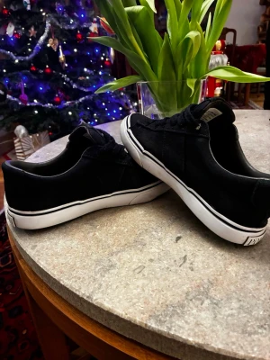 Svarta sneakers från Polo Ralph Lauren - Snygga svarta sneakers från Polo Ralph Lauren med klassisk logga på sidan och POLO-tryck på hälen. Skorna har snörning, vit platt sula och rund tå. Materialet är canvas med detaljer i skinn. Perfekta för dig som gillar stilrena och tidlösa sneakers.