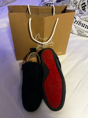 Christian louboutin - Säljer ett par svarta sneakers från Christian Louboutin med klassisk röd sula och snygg signatur på undersidan. Skorna har rund tå, snörning och är tillverkade i skinn med textilinslag. Perfekt för dig som vill ha något exklusivt och stilrent i garderoben. Nästintill nya använda en gång 