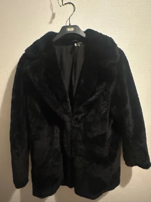 Svart pälsjacka från Divided H&M - Säljer en svart pälsjacka från Divided H&M i storlek M. Jackan har en klassisk krage, rak passform och är helsvart med mjukt fuskpälsmaterial. Perfekt för dig som vill ha en snygg och varm jacka med lite lyxig känsla.