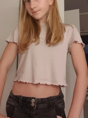 Ljusrosa/lila croppad topp från H&M Divided - Säljer en ljusrosa/lila croppad topp från H&M Divided i storlek S. Toppen har korta ärmar och vågiga kanter vid ärmslut och nederkant för en söt touch. Perfekt till jeans eller kjol för en chill look.