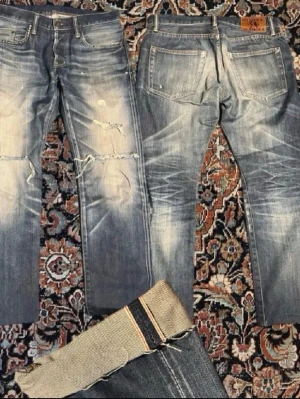 Selvedge Jeans - Säljer ett par klassiska Hysteric Glamour jeans i blå tvätt med coola slitningar och trasiga detaljer på knäna. Jeansen har raka ben och rå kant. Säljer billigare eftersom jag har klippt där nere. Hör av vid funderingar! Midjan är 40cm, längden är 90cm o benöppningen är 18.5cm
