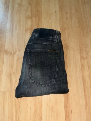 Nudie Jeans - Säljer ett par mörk gråa jeans från Nudie Jeans i modellen High Kai. Midja 32cm, längd 105cm. JAG SKICKAR EJ FLER BILDER NÄR JAG BÄR JEANSEN! för bättre inblick i passformen rekommenderar jag att googla på modellnamnet. För storleksguide kolla måtten noggrant då jeansen alltid kan vara uppsydda heller krympta och jag ej tar emot returer :) s5,3