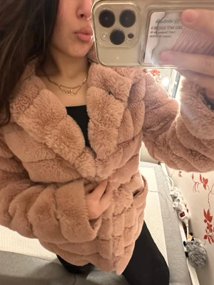 Beige fluffig pälsjacka - Supermjuk och fluffig beige pälsjacka med bred krage och markerade sömmar. Jackan har en oversized känsla och är perfekt för kalla dagar. Den är helfärgad och har långa ärmar, vilket gör den extra mysig och varm.