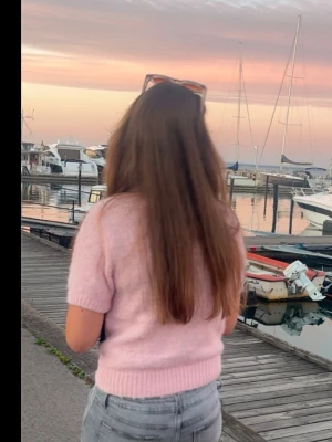 Ljusrosa stickad kortärmad topp - Säljer en ljusrosa stickad topp med korta ärmar och ribbad kant vid midjan och ärmslut. Mjuk och skön känsla, passar dig som gillar en söt och avslappnad stil.