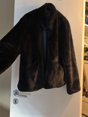 Svart pälsjacka från ONLY XL - Mjuk och fluffig svart pälsjacka från ONLY i storlek XL. Jackan har en klassisk krage, långa ärmar och knäppning framtill. Insidan är fodrad med slätt tyg och jackan har en loose passform. Har ett litet hål i fickan. 
