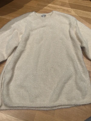 Glittrig beige stickad tröja H&M - Säljer en beige stickad tröja från H&M i storlek M. Tröjan har ett glittrigt material och långärmad design med rund hals. Den har en slits på sidan för extra stilpoäng och är perfekt för dig som gillar mjuka och mysiga plagg med lite extra shine.