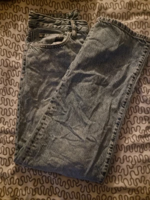 Gråblå raka jeans från ginatricot  - Säljer ett par klassiska gråblå jeans från ginatricot med raka ben och femficksmodell. Jeansen har en snygg tvättad look och läderpatch bak i midjan. Perfekta för dig som gillar en enkel och tidlös stil.