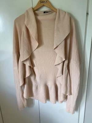 Ljusrosa volangkofta från Gina Tricot - .Supersnygg ljusrosa kofta från Gina Tricot i storlek L. Koftan har långa ärmar, bred krage och coola volangdetaljer längs fram och nederkant. Mjuk stickad kvalitet som är perfekt för lager-på-lager och chill vibes.