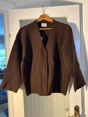 Brun cardigan från ÀVORA XS/S - Snygg cardigan från ÀVORA i rak modell med v-ringning och två fickor framtill. Koftan är tillverkad i ett mjukt material och har breda ärmar som ger en avslappnad look. 